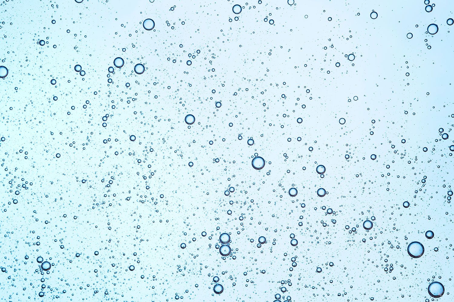 Zahlreiche kleine und größere Luftblasen steigen in einer klaren, hellblauen Flüssigkeit auf. Die Blasen wirken gleichmäßig verteilt und erinnern an Geltexturen oder Wasser in Nahaufnahme. Das Bild vermittelt Frische, Leichtigkeit und Feuchtigkeit.